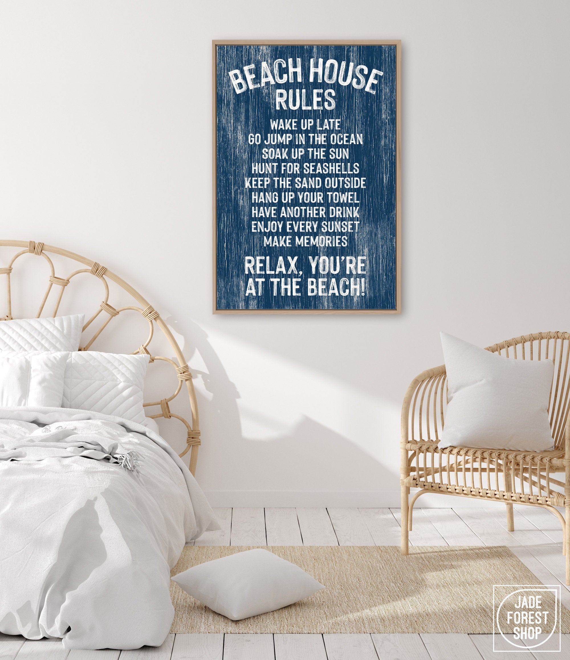 A cozy beach-themed room features a rattan bed, chair, coastal wall art, and a charming "Beach House Rules Sign" made of painted wood with a nautical design displayed on the wall.