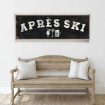 a wooden bench with two striped pillows, and above it is a framed sign with the text "APRÈS SKI" and various icons representing drinks and skiing equipment.