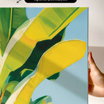 The image is a vibrant abstract painting featuring a large yellow leaf with green and yellow accents, set against a blue background.