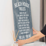 Someone holds the Harbor Blue Beach House Rules Sign, made of painted wood, ideal as coastal wall art, next to a vase with reed diffusers.