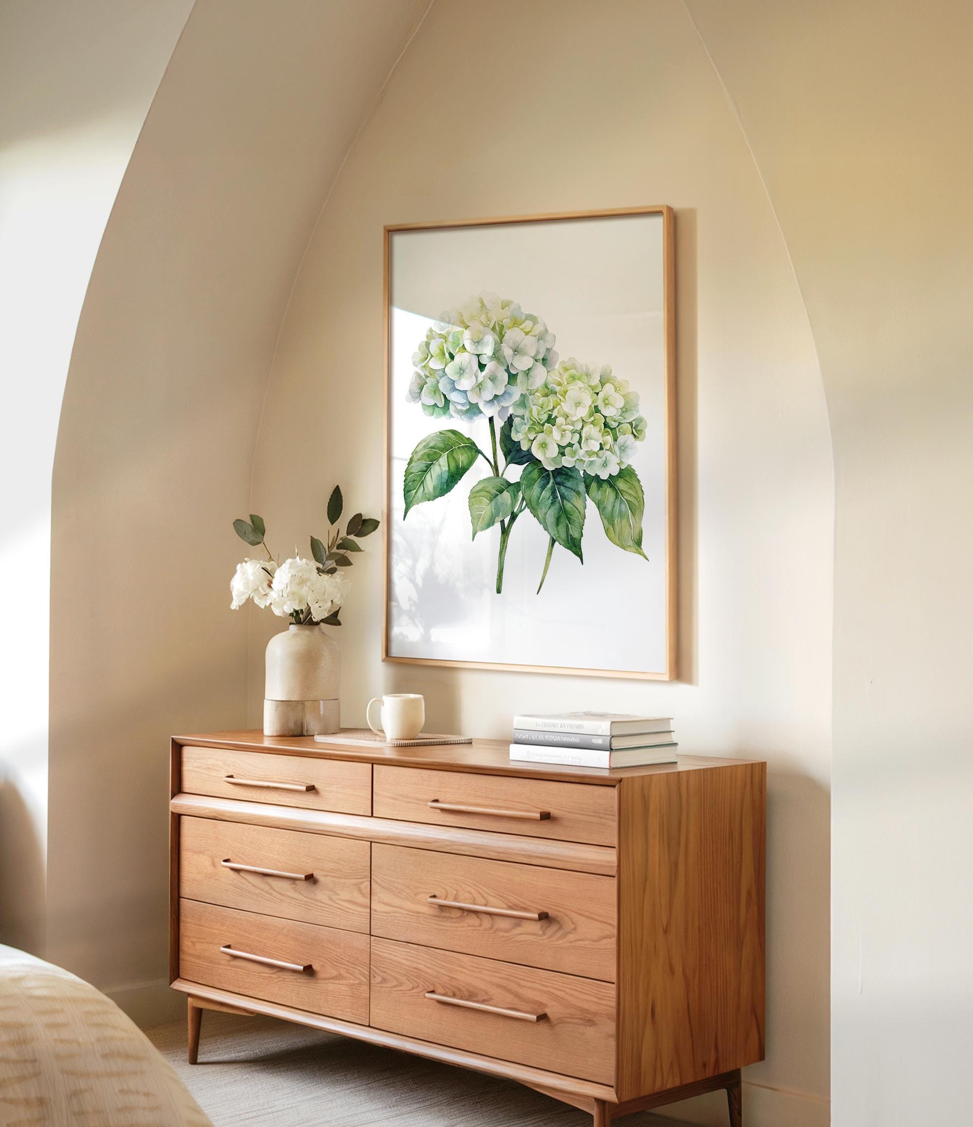 a wooden dresser with a framed painting of green hydrangeas hanging on the wall above it. The dresser has six drawers and a vase with white flowers on top.