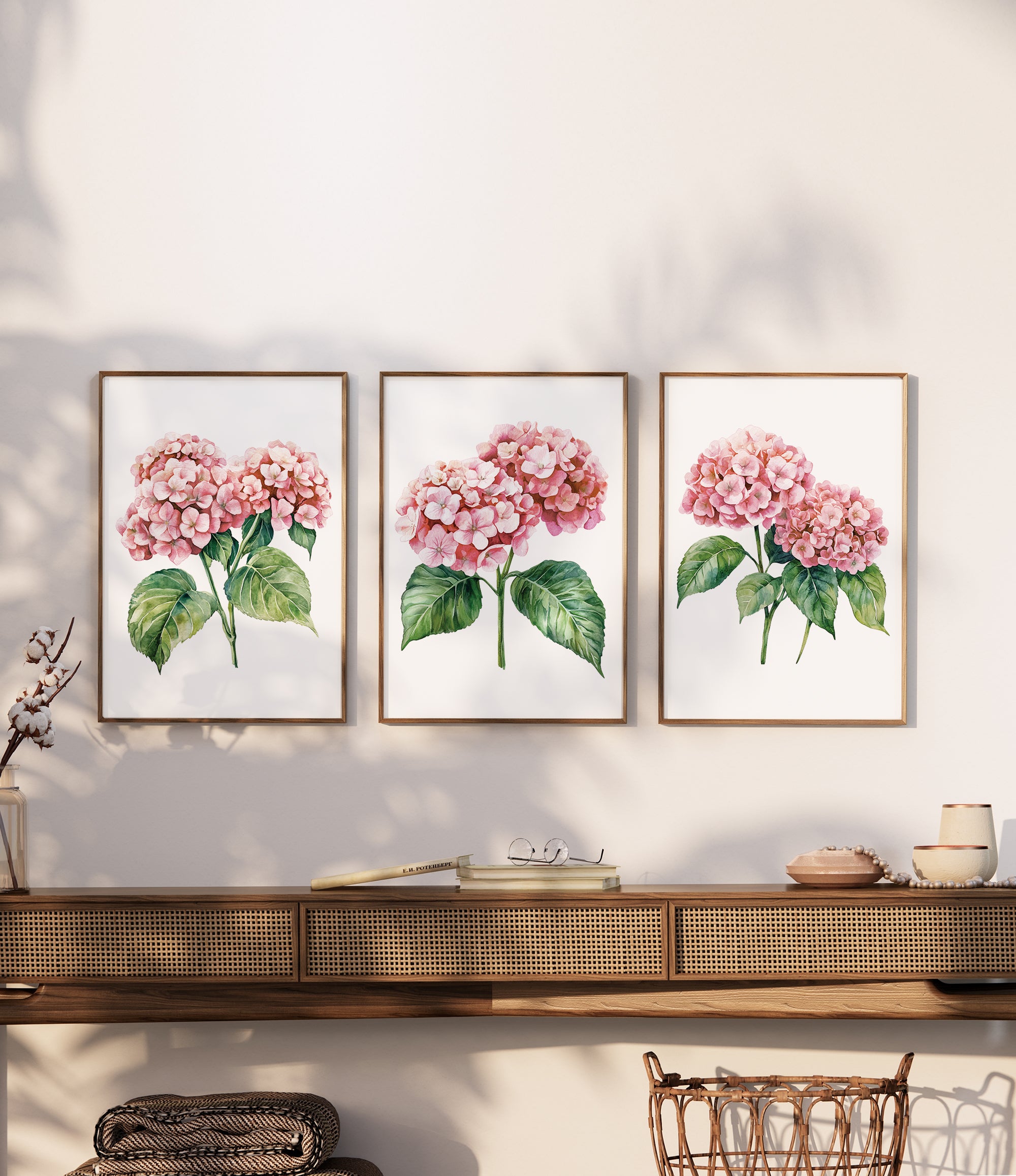 three framed watercolor paintings of pink hydrangeas hanging on a wall above a wooden shelf.