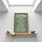 a framed sign with a list of rules for a lake house, placed on a shelf above a bowl.