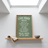 a framed sign with a list of rules for a lake house, placed on a shelf above a bowl.