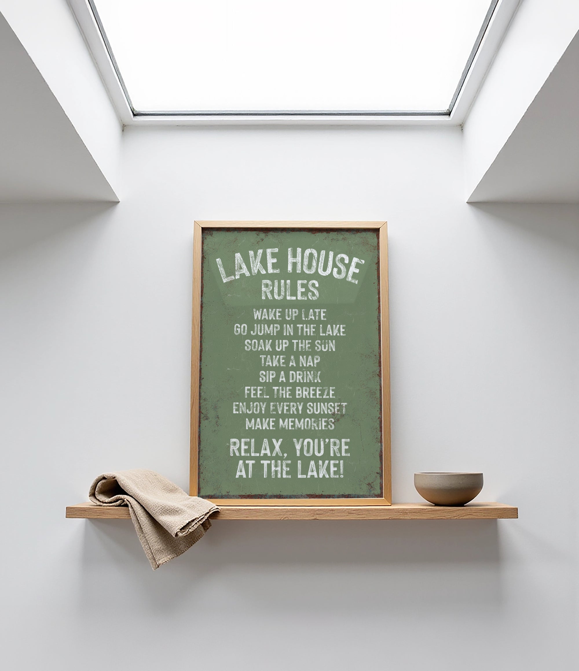 a framed sign with a list of rules for a lake house, placed on a shelf above a bowl.