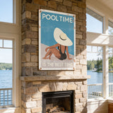a fireplace with a framed poster of a woman in a hat and swimsuit above it, and a scenic view of a lake and trees outside the window.
