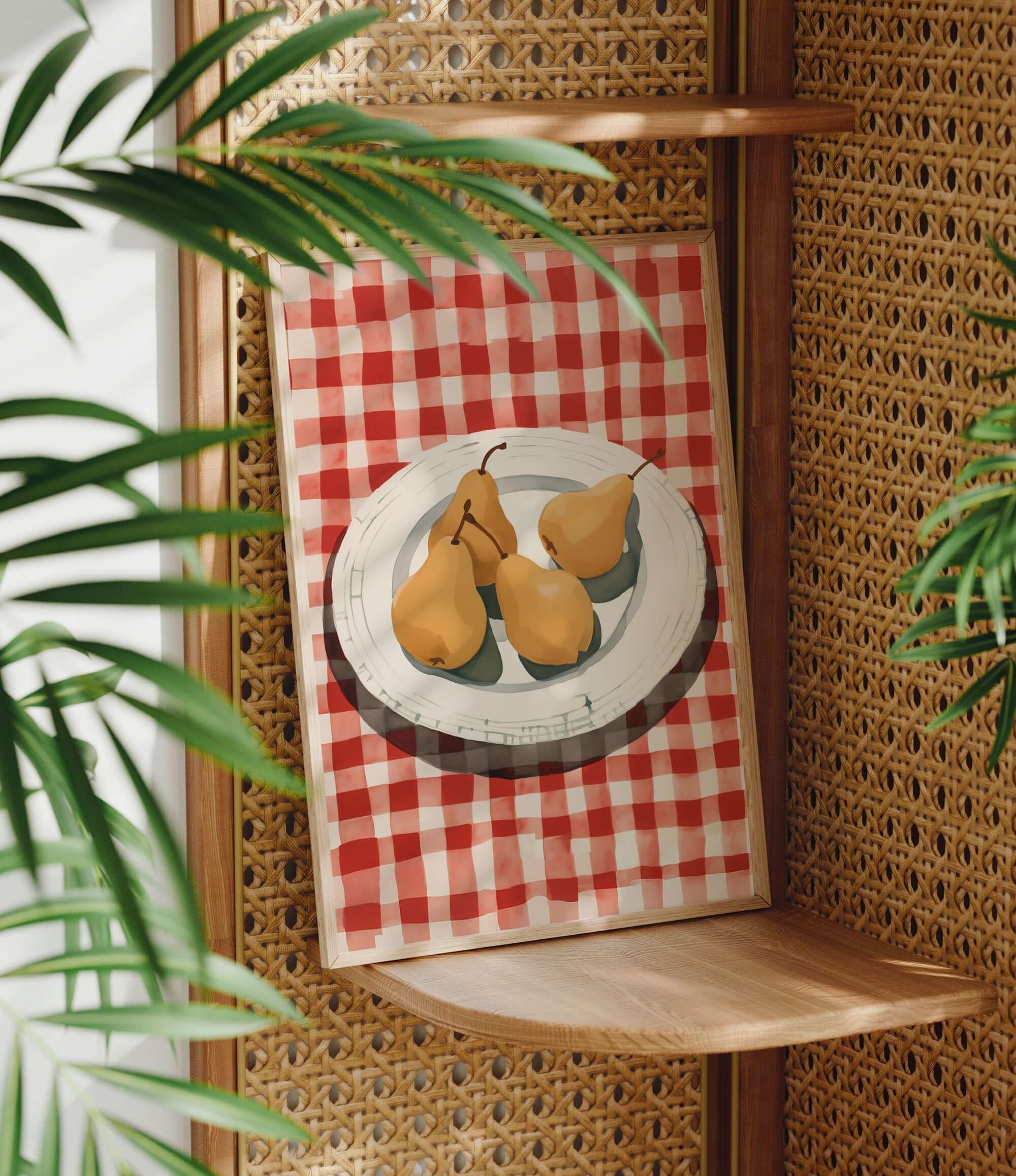 A framed painting of three pears on a red and white checkered tablecloth is displayed on a wooden shelf, with a woven plant in the foreground.