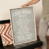 A person is holding up a framed sign with text on it, which appears to be a list of rules or instructions for a lake house.
