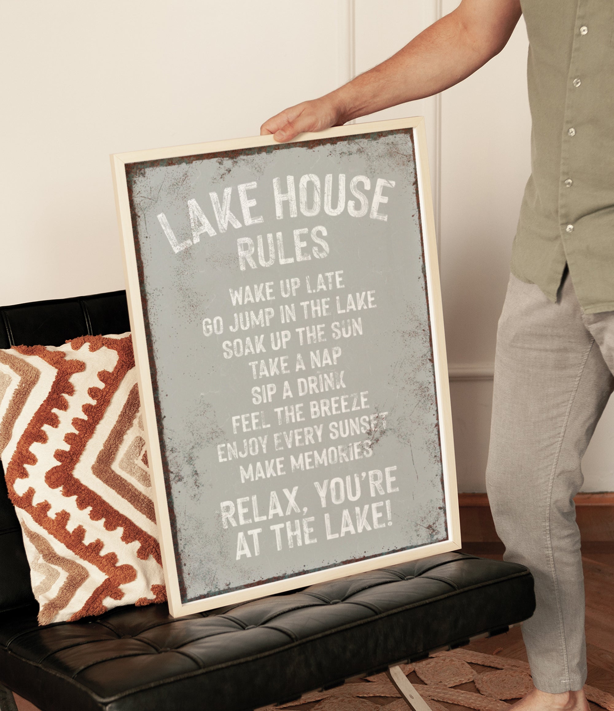 A person is holding up a framed sign with text on it, which appears to be a list of rules or instructions for a lake house.