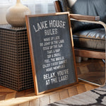 A chalkboard sign with the text "LAKE HOUSE RULES" written on it, placed on a wooden floor next to a chair.