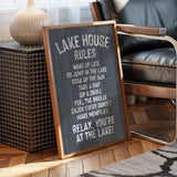 A chalkboard sign with the text "LAKE HOUSE RULES" written on it, placed on a wooden floor next to a chair.