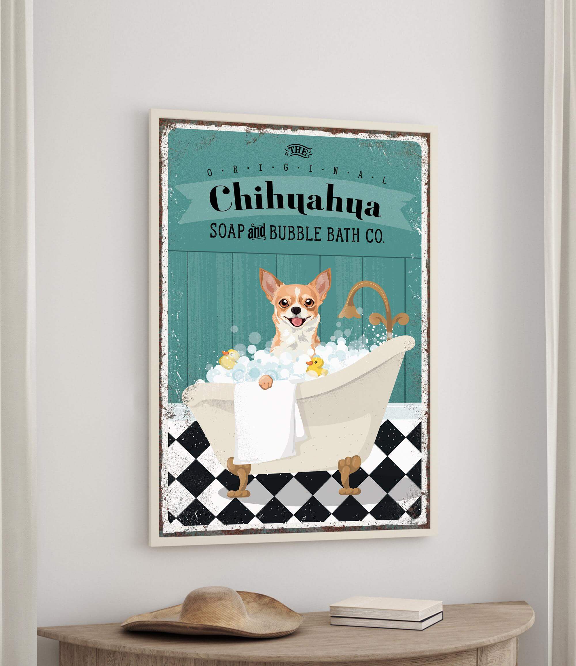 A framed poster of a Chihuahua dog sitting in a bathtub, surrounded by bubbles, with a towel and a book on a table below it.