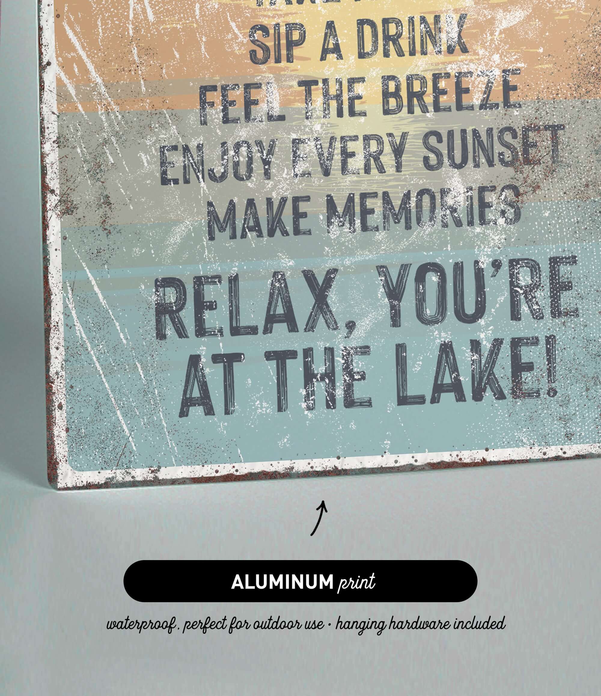 The image is a sign with text that reads "Sip a Drink, Feel the Breeze, Enjoy Every Sunset, Make Memories, Relax, You're at the Lake!" The sign is made of metal and has a black arrow pointing to it.