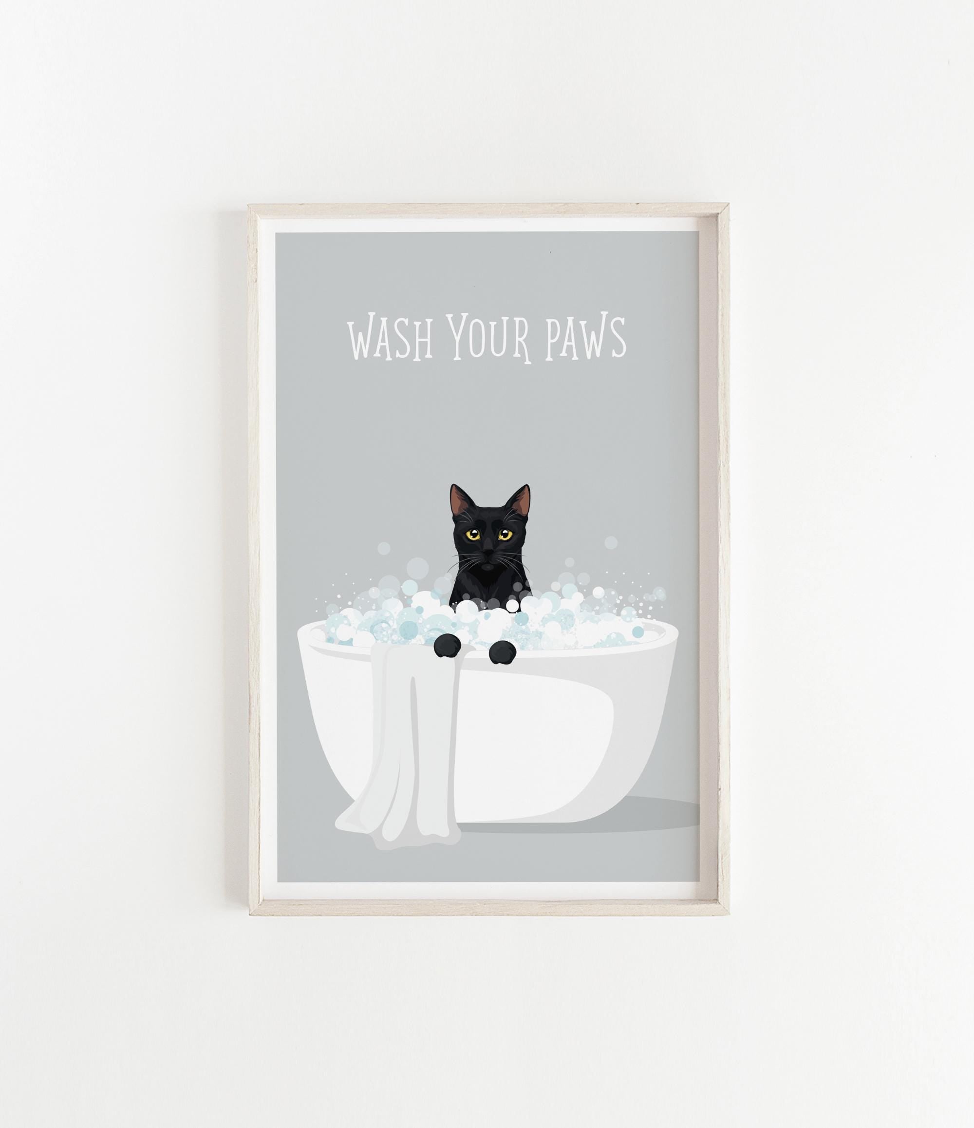 A framed poster with a black cat sitting in a white bathtub filled with bubbles, with the text "WASH YOUR PAWS" displayed above the cat.