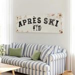 a living room with a striped couch, a coffee table, and a large sign that says "APRÈS SKI" hanging on the wall.
