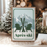 A framed print with a winter scene featuring two green Adirondack chairs and skis, set against a snowy mountain backdrop.