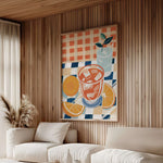 a cozy living room with a large, colorful painting of a drink on the wall, featuring a glass, orange slices, and a potted plant. The room has a wooden wall and a white sofa, creating a warm and inviting atmosphere.