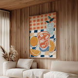 a cozy living room with a large, colorful painting of a drink on the wall, featuring a glass, orange slices, and a potted plant. The room has a wooden wall and a white sofa, creating a warm and inviting atmosphere.