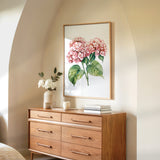 a wooden dresser with a framed painting of pink flowers hanging on the wall above it. The dresser has six drawers and a vase of white flowers on top.