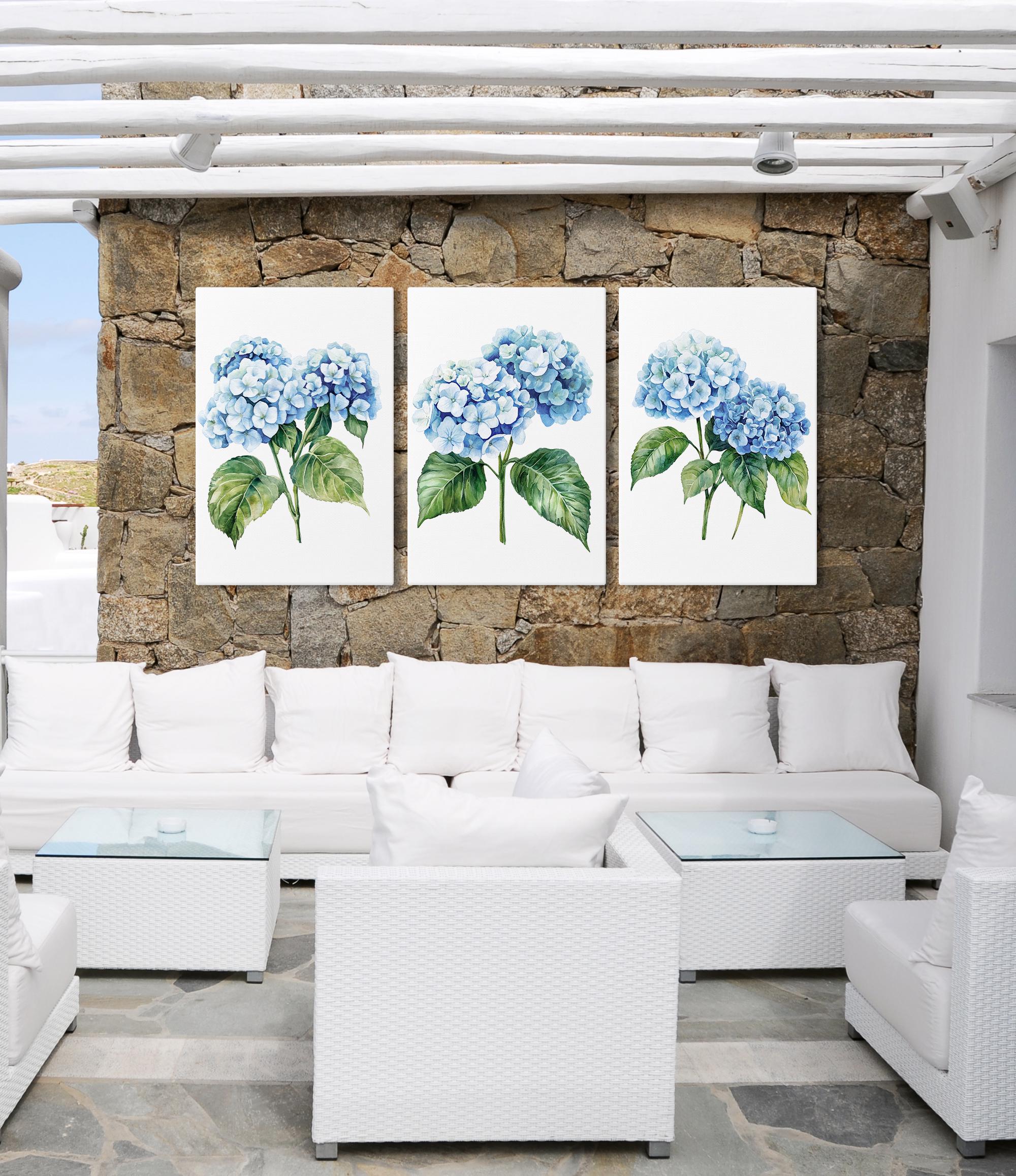 a cozy outdoor seating area with white wicker furniture and a stone wall backdrop. Three framed paintings of blue hydrangeas are displayed on the wall, creating a harmonious and visually appealing atmosphere.