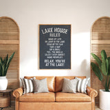 a cozy living room with a brown leather couch, a potted plant, and a chalkboard sign that reads "Lake House Rules" in a black and white color scheme.