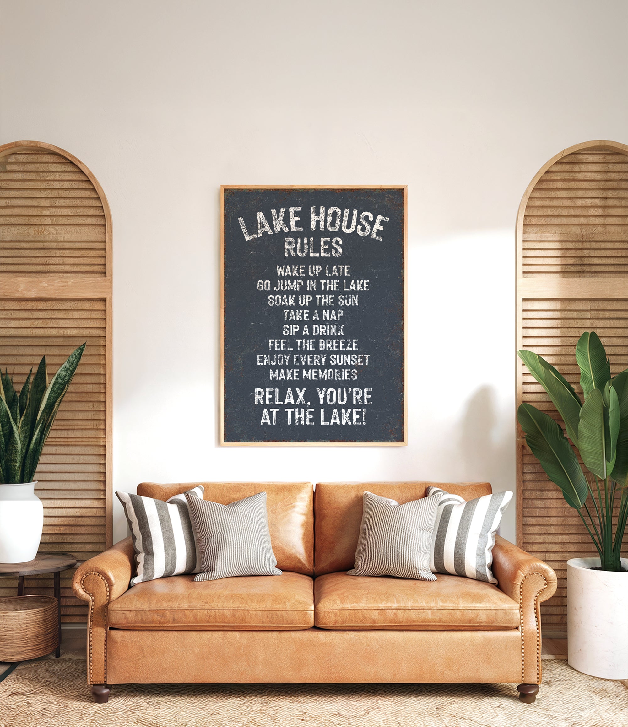a cozy living room with a brown leather couch, a potted plant, and a chalkboard sign that reads "Lake House Rules" in a black and white color scheme.