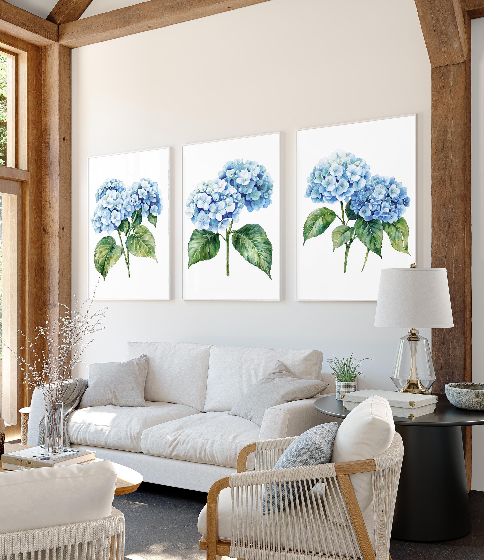 a cozy living room with a white sofa, a wooden coffee table, and three framed paintings of blue hydrangeas on the wall.