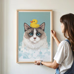 A woman is hanging a framed picture of a cat with a yellow rubber duck on its head.
