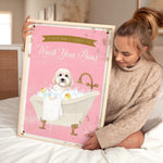 A woman is sitting on a bed holding a framed poster with a dog in a bathtub.