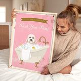 A woman is sitting on a bed holding a framed poster with a dog in a bathtub.
