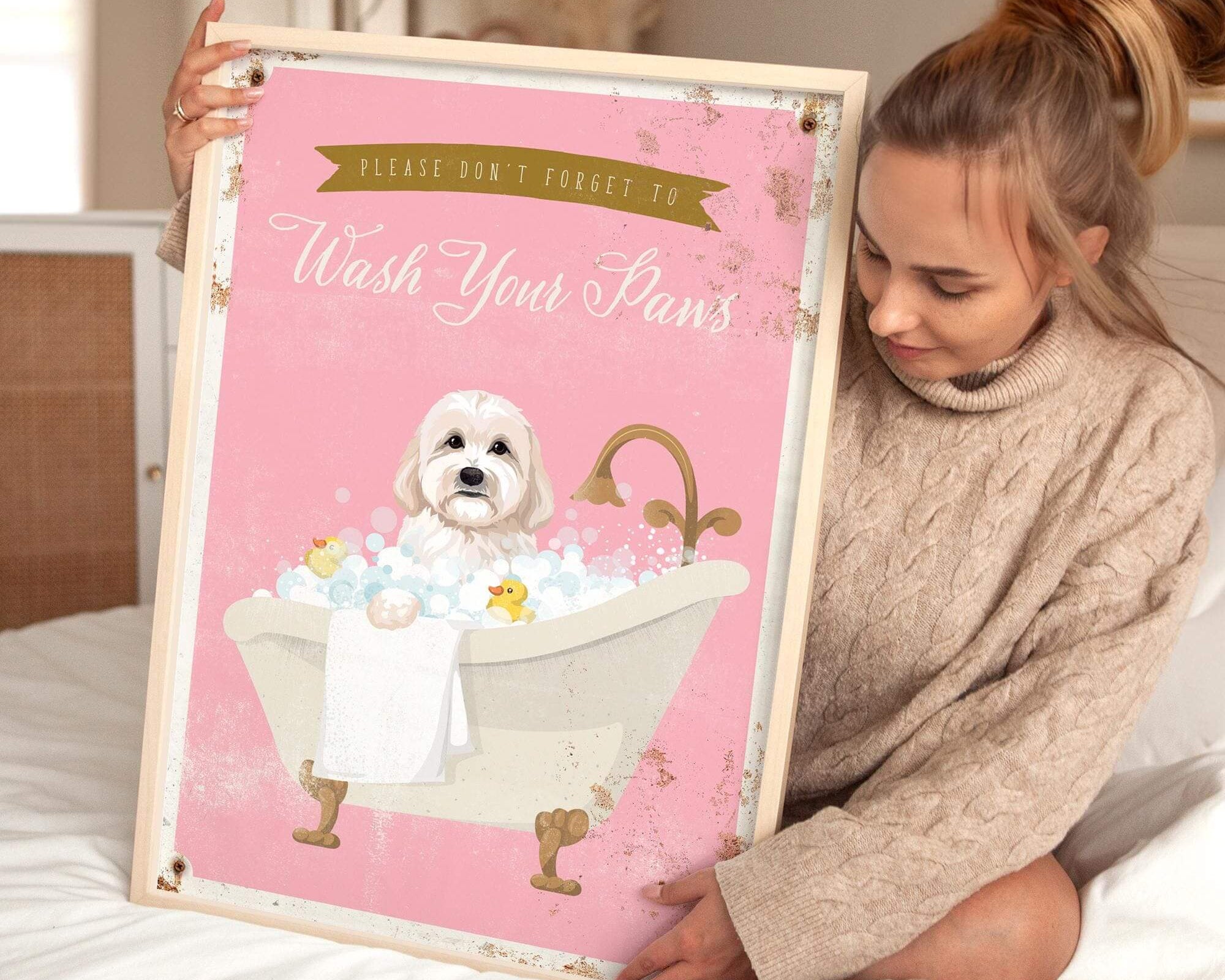 A woman is sitting on a bed holding a framed poster with a dog in a bathtub.