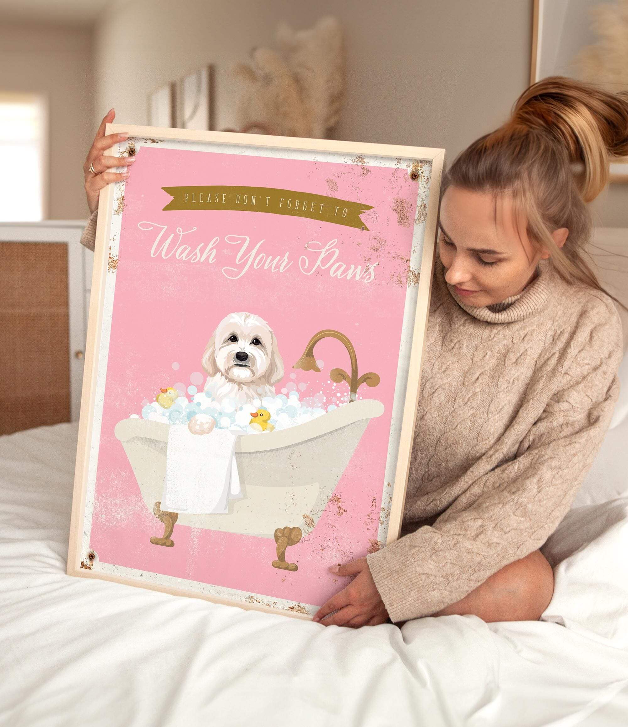 A woman is sitting on a bed holding a framed poster with a dog in a bathtub.