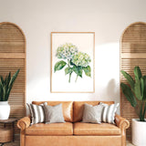 a living room with a brown leather sofa, a framed watercolor painting of green hydrangeas, and two potted plants on either side of the sofa.