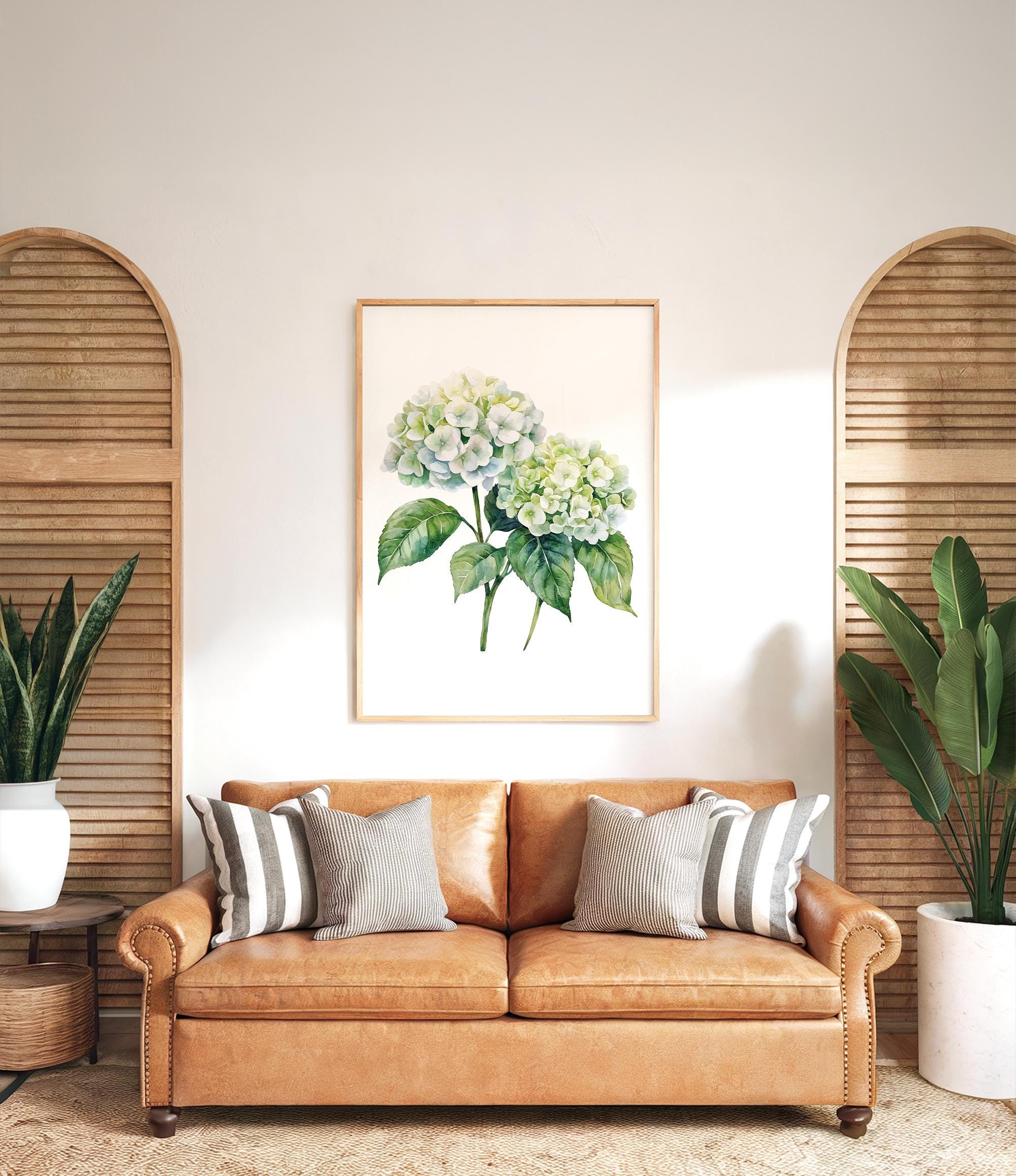 a living room with a brown leather sofa, a framed watercolor painting of green hydrangeas, and two potted plants on either side of the sofa.
