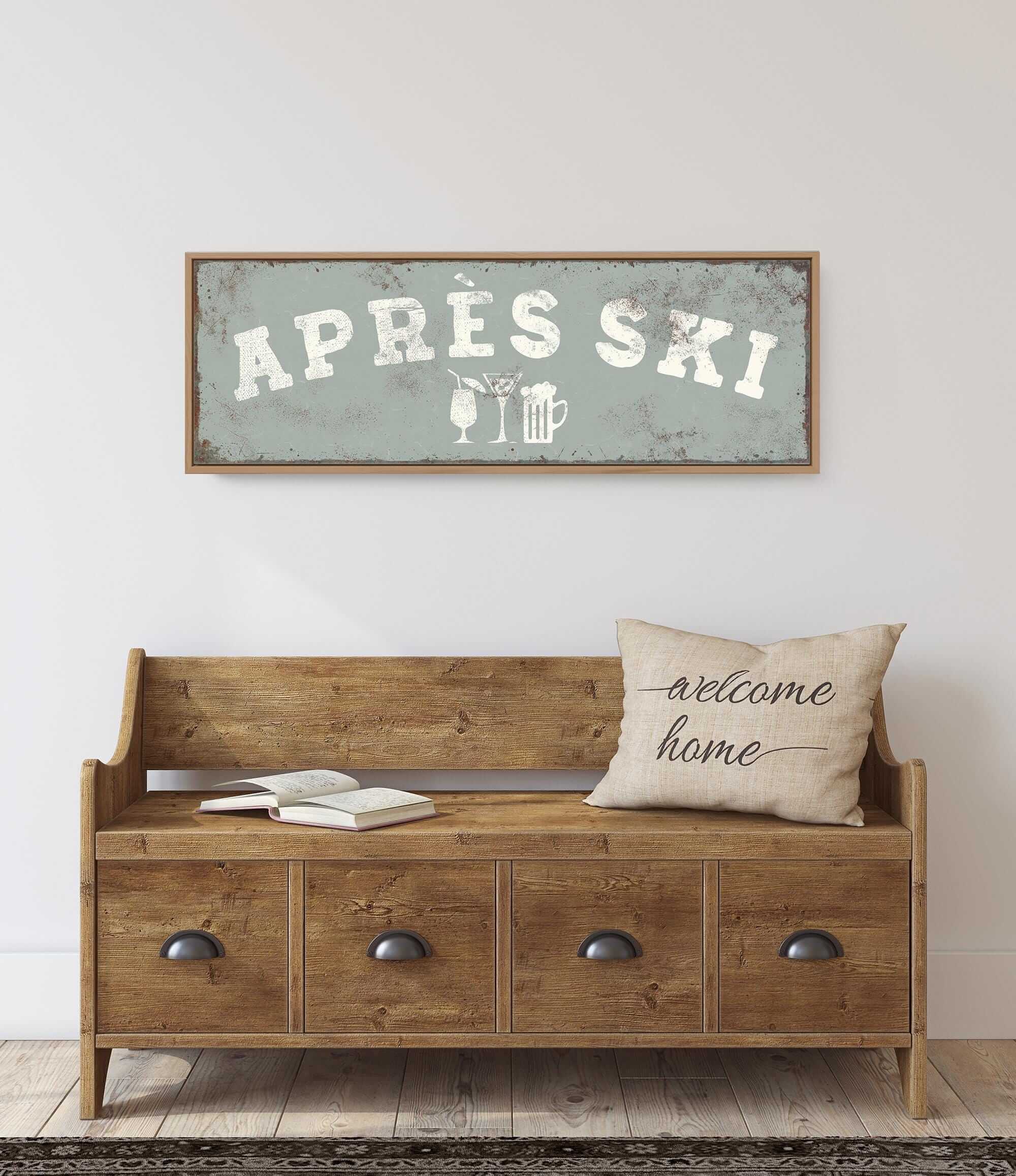 a wooden bench with a "welcome home" pillow on it, set against a white wall. Above the bench, there is a framed sign that says "APRÈS SKI".