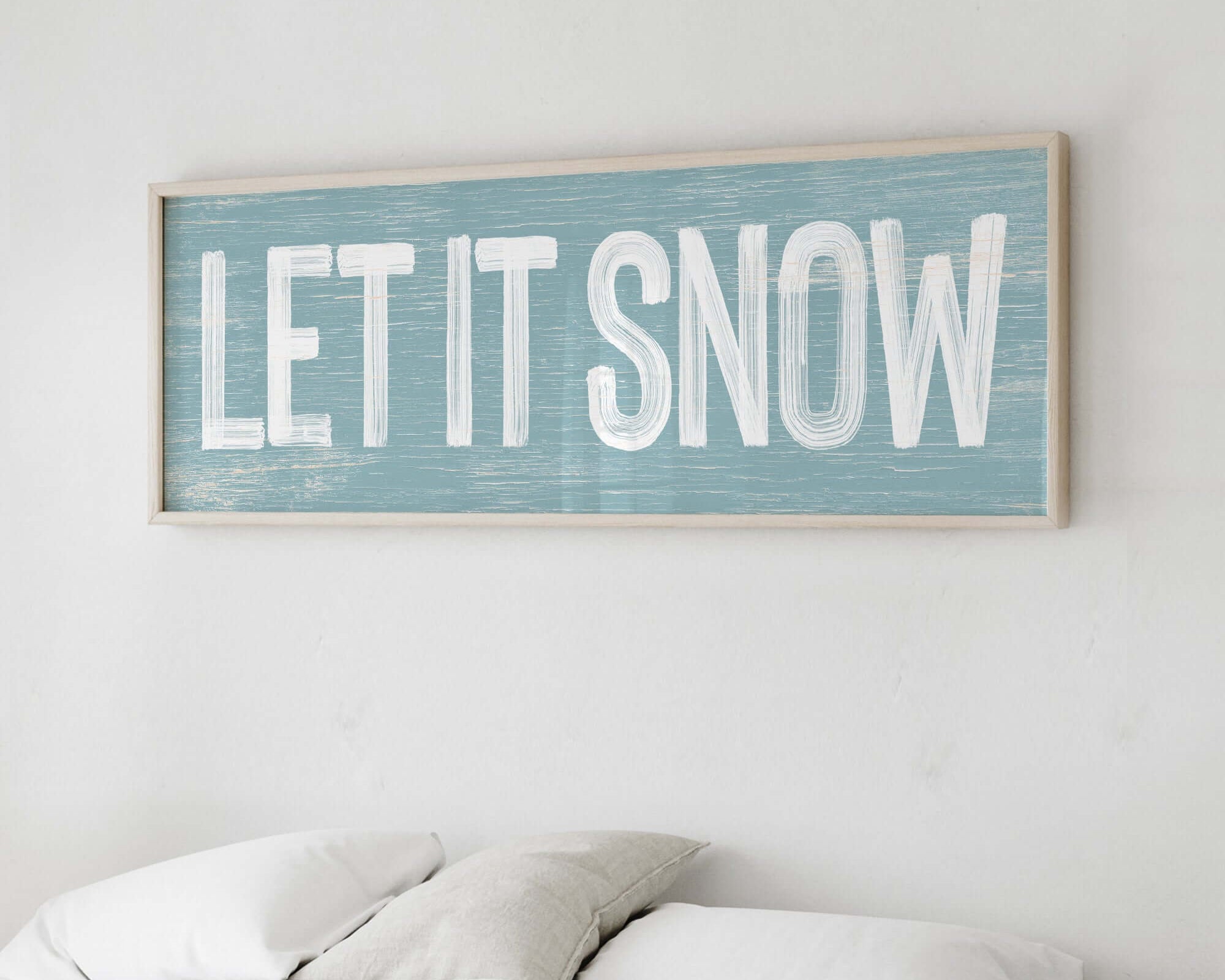 a wooden sign that says let it snow on a wall above a bed