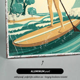 A woman is standing on a surfboard and paddling through the waves, with a beach and trees in the background.