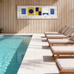 a serene outdoor setting with a swimming pool, wooden lounge chairs, and a wooden wall with a framed artwork depicting nautical symbols.