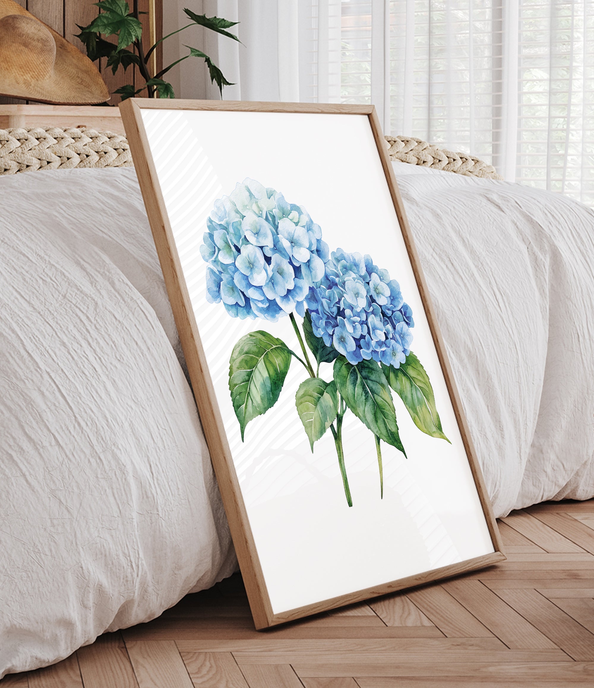 A framed watercolor painting of blue hydrangea flowers is displayed on a wooden floor in a bedroom setting.