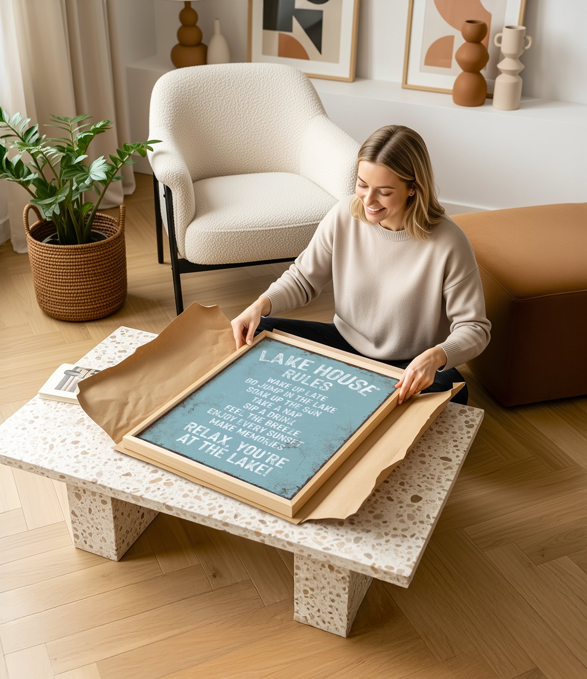 A woman is sitting on the floor in a living room, holding a framed sign with text on it.