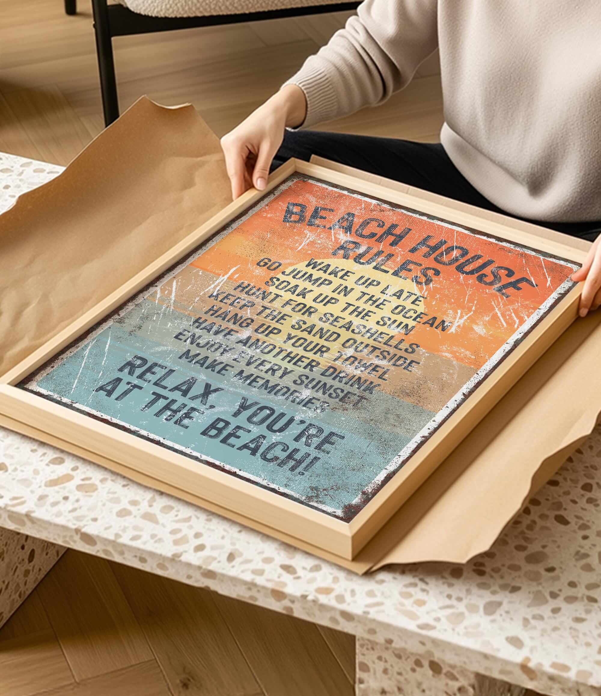 A person is holding a framed sign with the text "BEACH HOUSE RULES" on it, which appears to be a beach-themed decoration or sign.