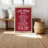 A red sign with white text that reads "LAKESHOUSE RULES" is displayed in a room with a wooden bench, a woven basket, and a rug.