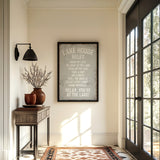 a hallway with a framed sign that reads "LAKESHORE RULES", a wooden table with a vase of branches, and a rug on the floor.