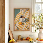 a cozy kitchen scene with a framed painting of a cup of coffee and a lemon on a striped tablecloth, surrounded by various kitchen items such as a cutting board, a bowl of fruit, and a vase of flowers.