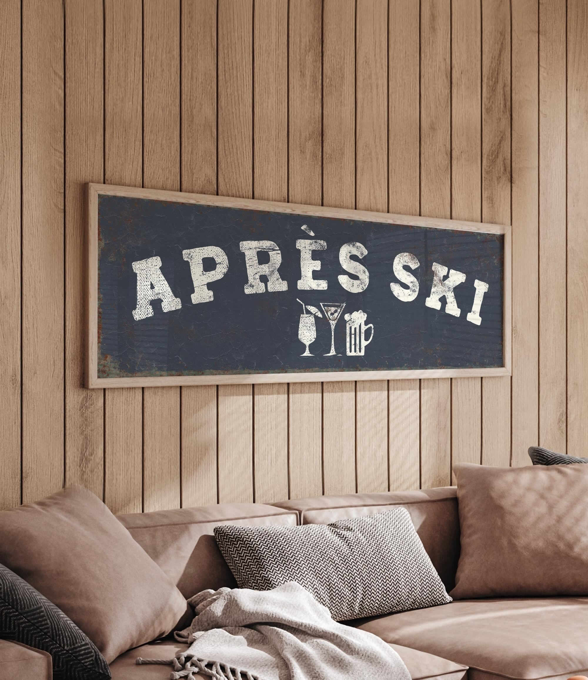 a cozy living room with a wooden wall and a comfortable couch. Above the couch, there is a framed sign that reads "APRÈS SKI", which appears to be a humorous take on skiing.