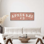 a living room with a white sofa, a wooden coffee table, and a decorative plant. Above the sofa, there is a large sign that says "APRES SKI".