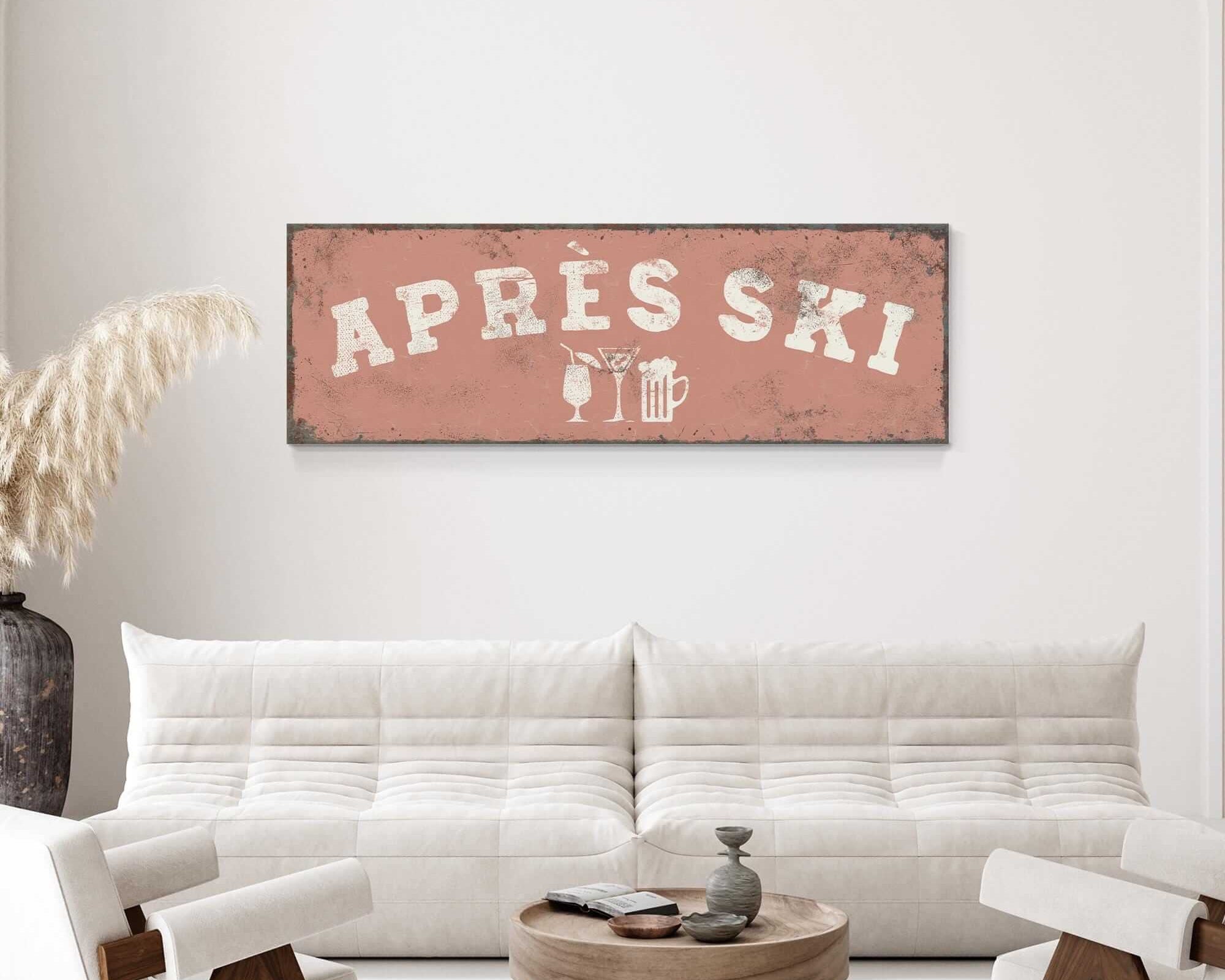 a living room with a white sofa, a wooden coffee table, and a decorative plant. Above the sofa, there is a large sign that says "APRES SKI".