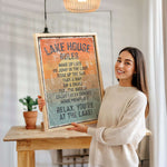 A woman is holding up a framed sign with a list of rules for a lake house, smiling and posing for the camera.