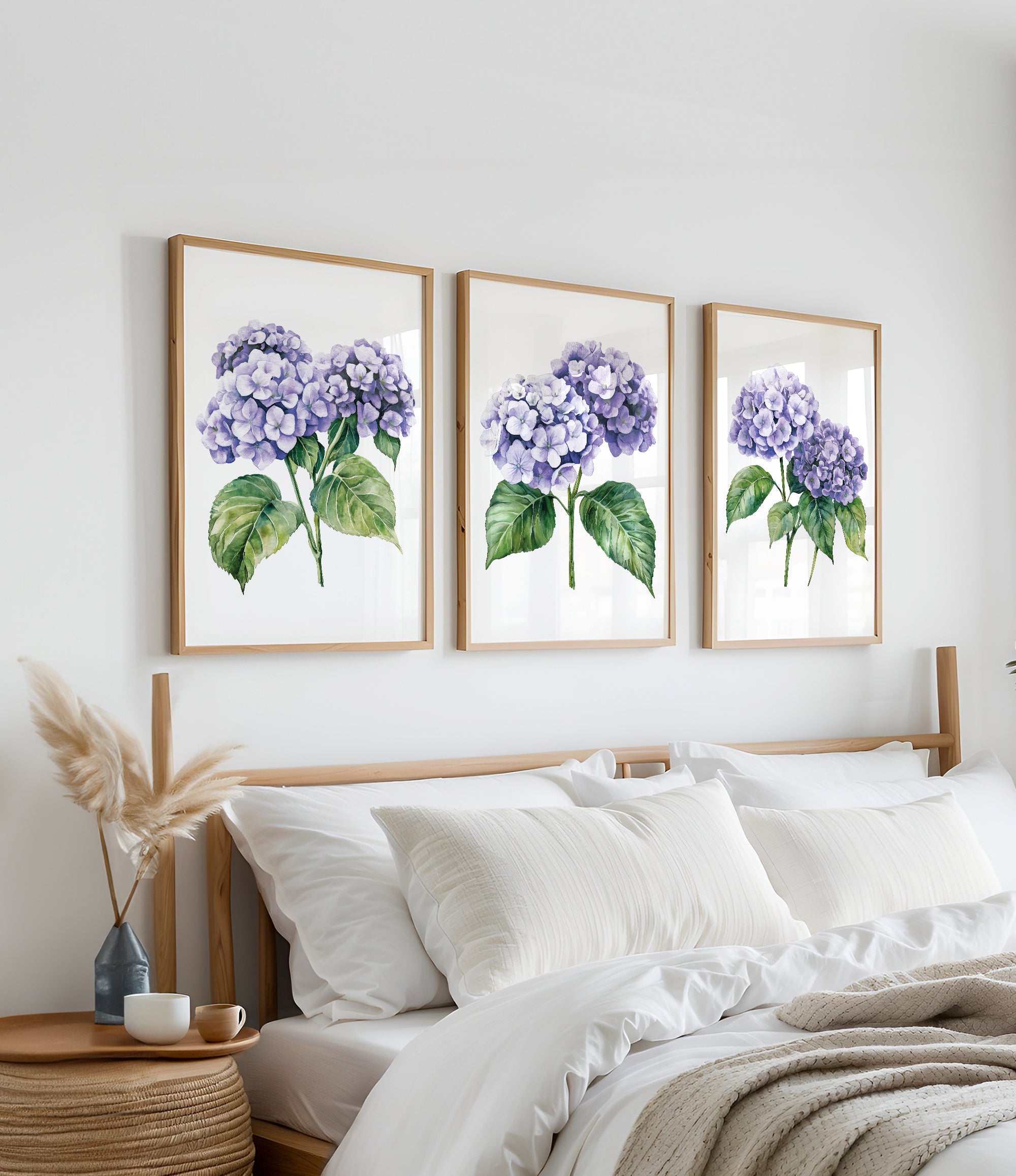 a bedroom with a bed, white pillows, and a wooden headboard. Above the bed, there are three framed watercolor paintings of purple hydrangeas hanging on the wall.