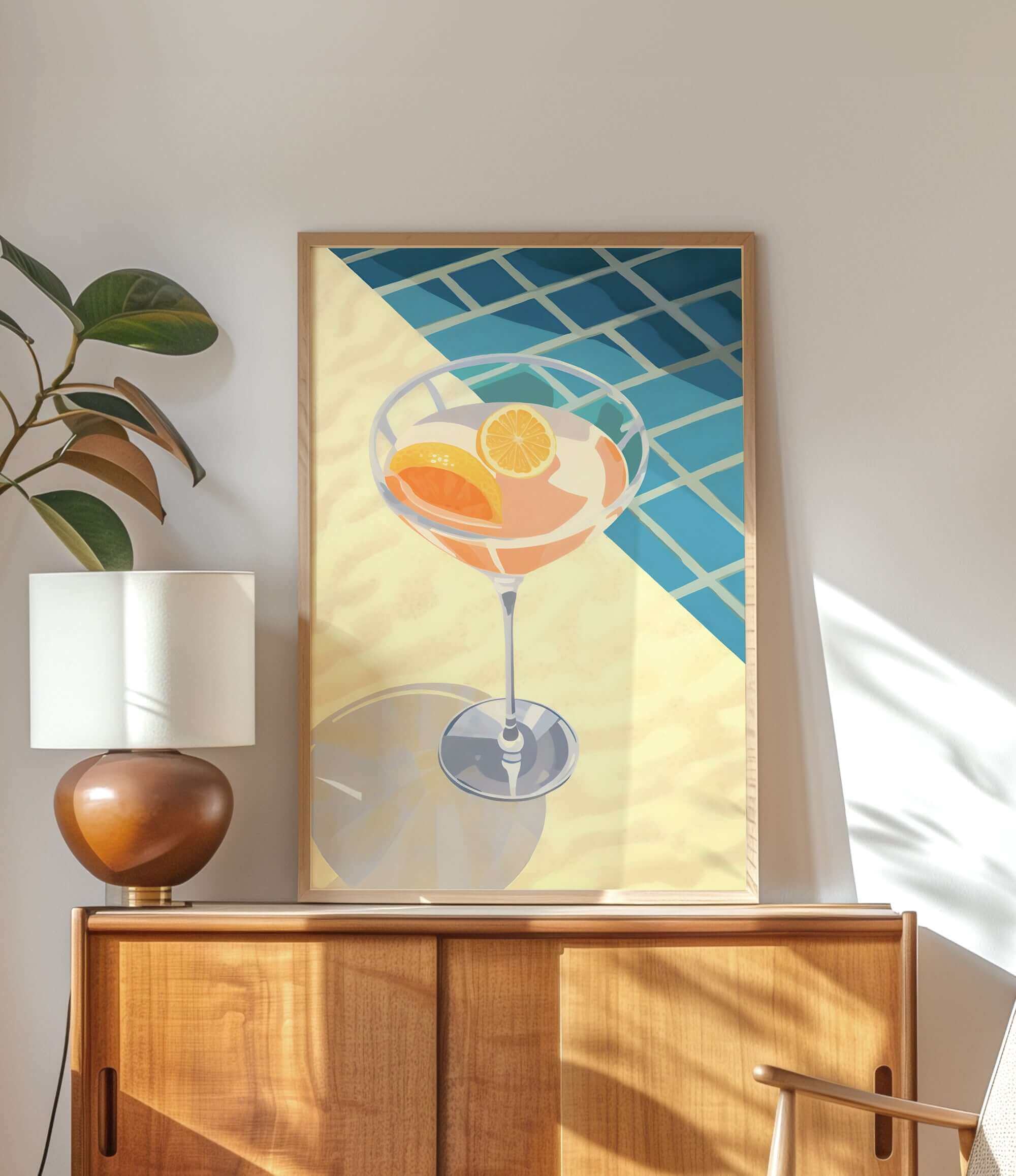 a framed illustration of a cocktail glass with orange slices, placed on a wooden cabinet or dresser.